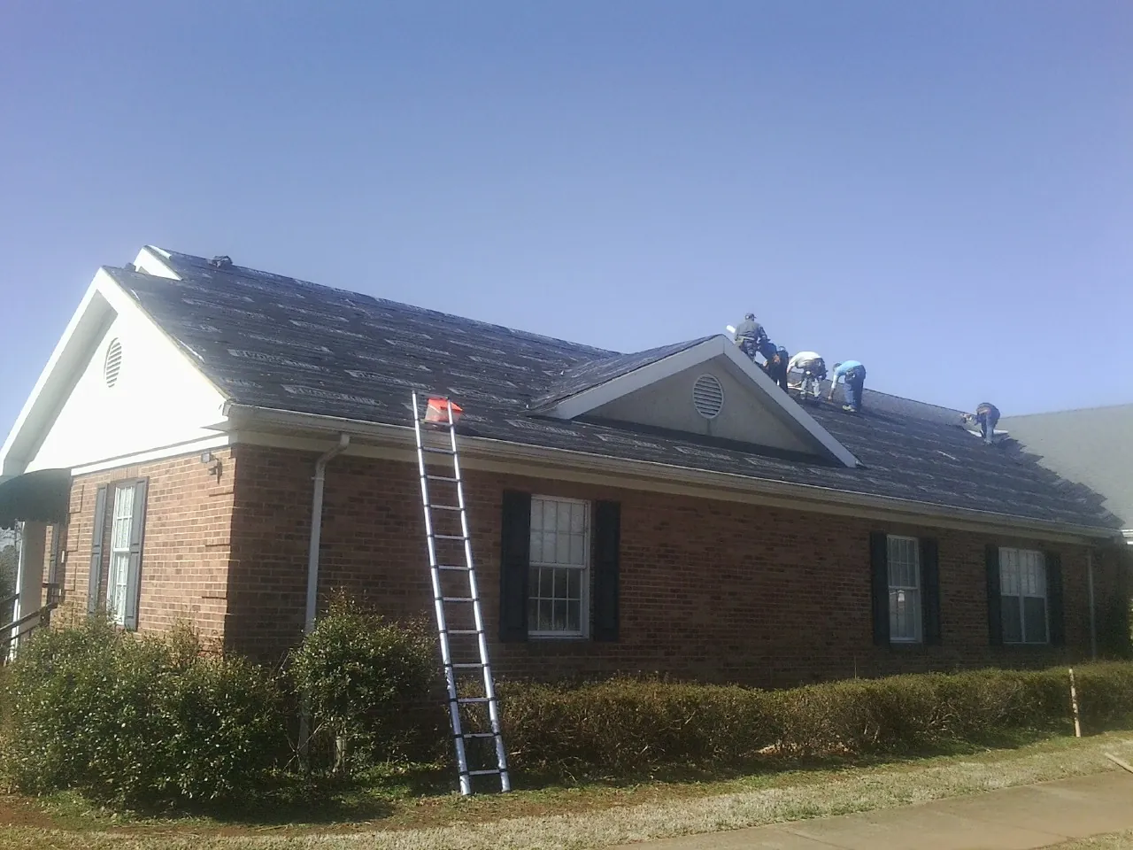Crew tearing shingles off a brick ranch roof with a ladder set — Emergency Roof Repair work by our crew in South Bound Brook