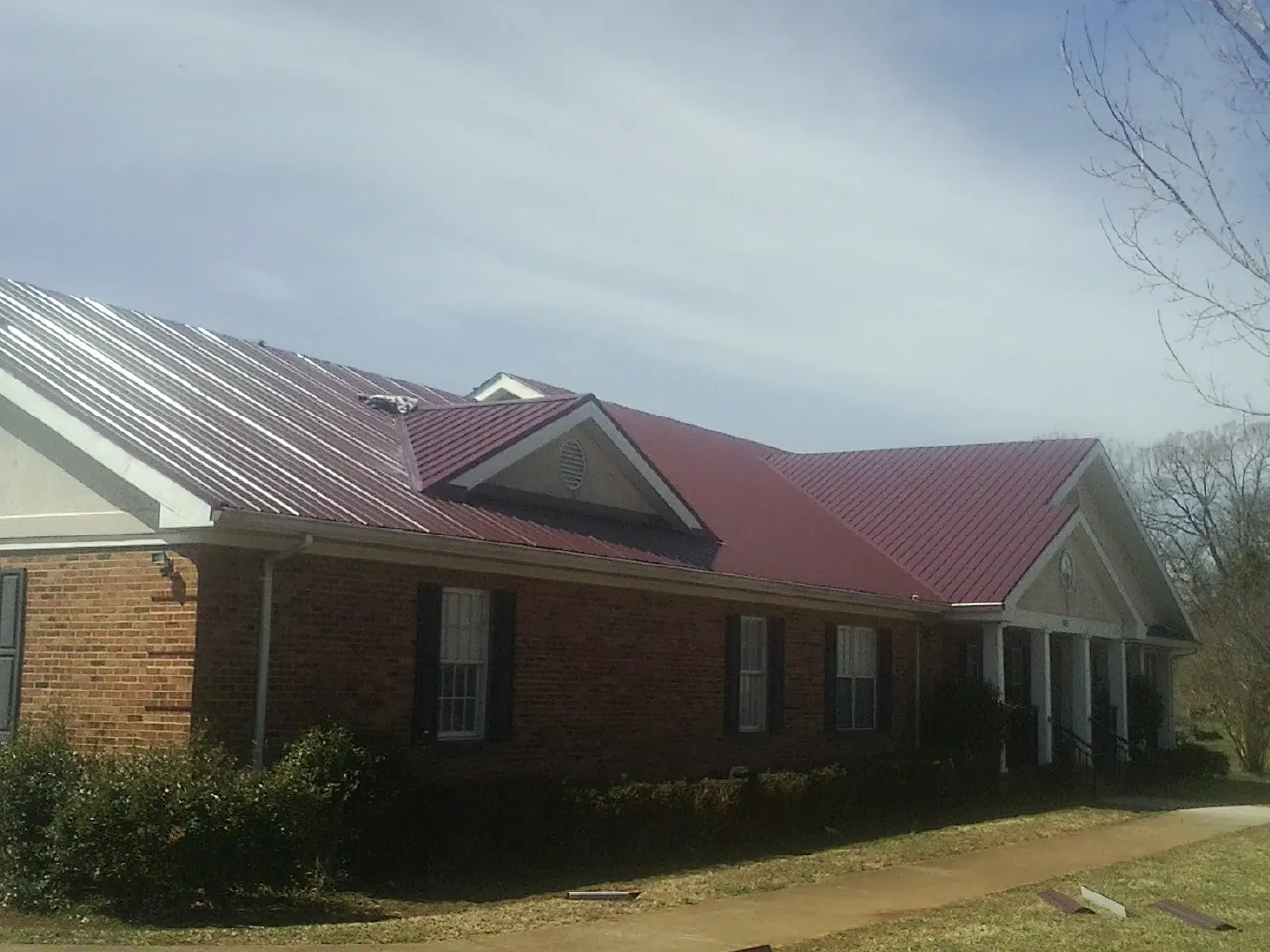 Red metal roof with gabled entries on a long brick building, from a Hail Damage Roof Repair job in South Bound Brook