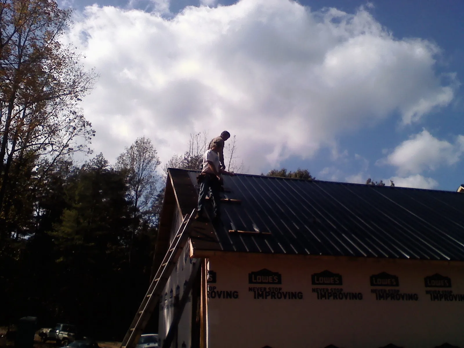 Roofer fastening dark metal panels high against a cloudy sky, from a Roof Inspection job in South Bound Brook