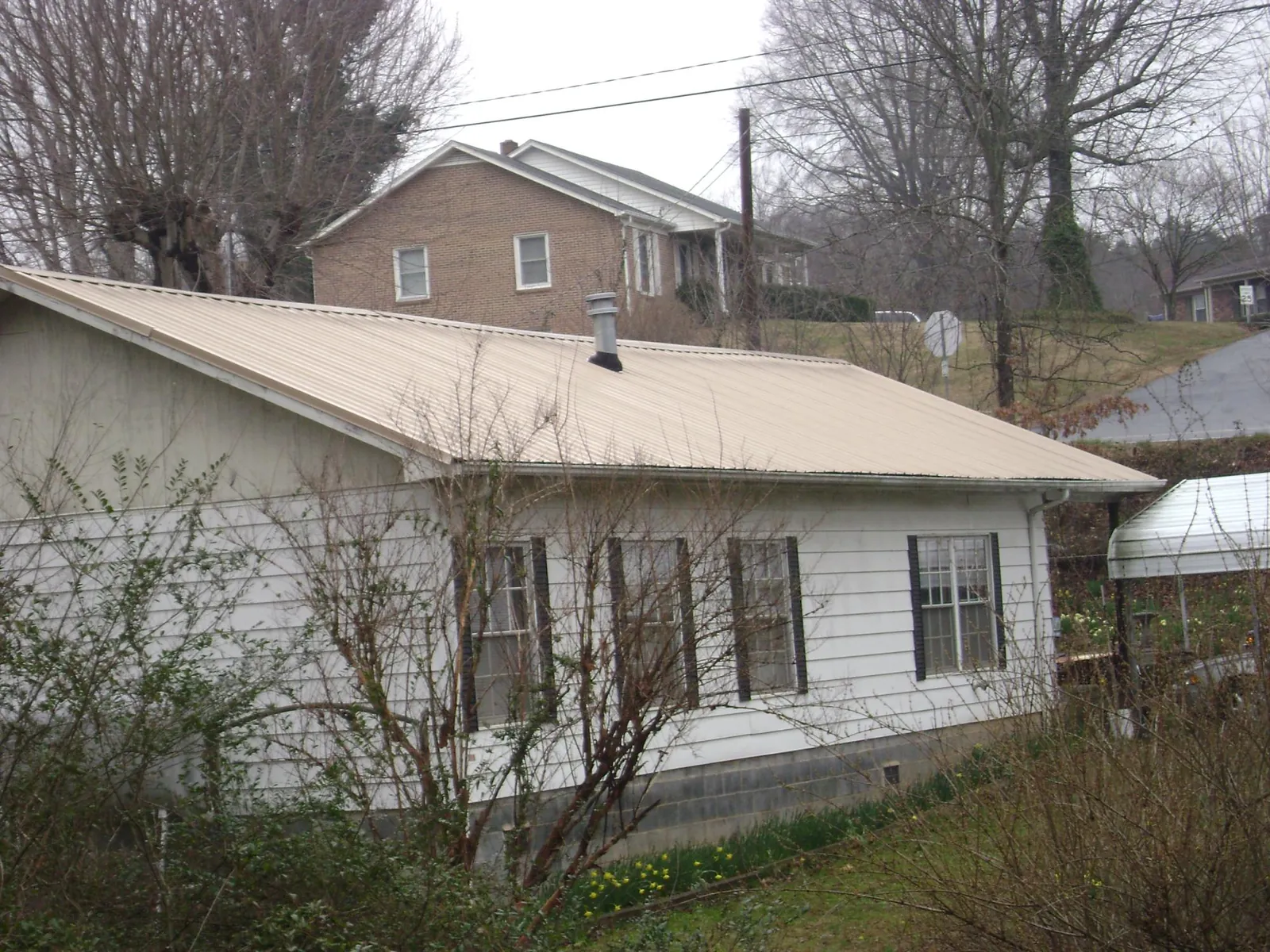 Tan metal roof on a white sided house set into a hillside — Commercial Roofing by Roofing Brothers in South Bound Brook